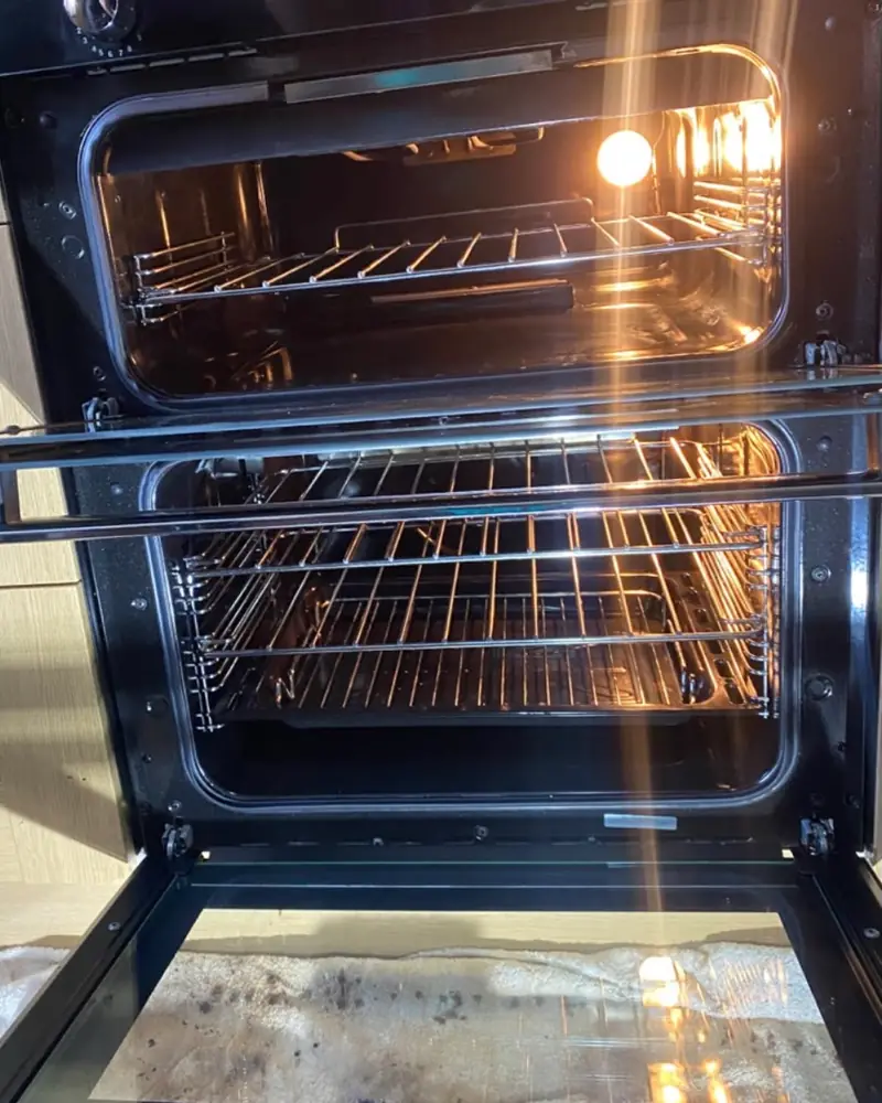 The same double oven after cleaning, both cavities lit, with clean racks, shelf runners and enamel