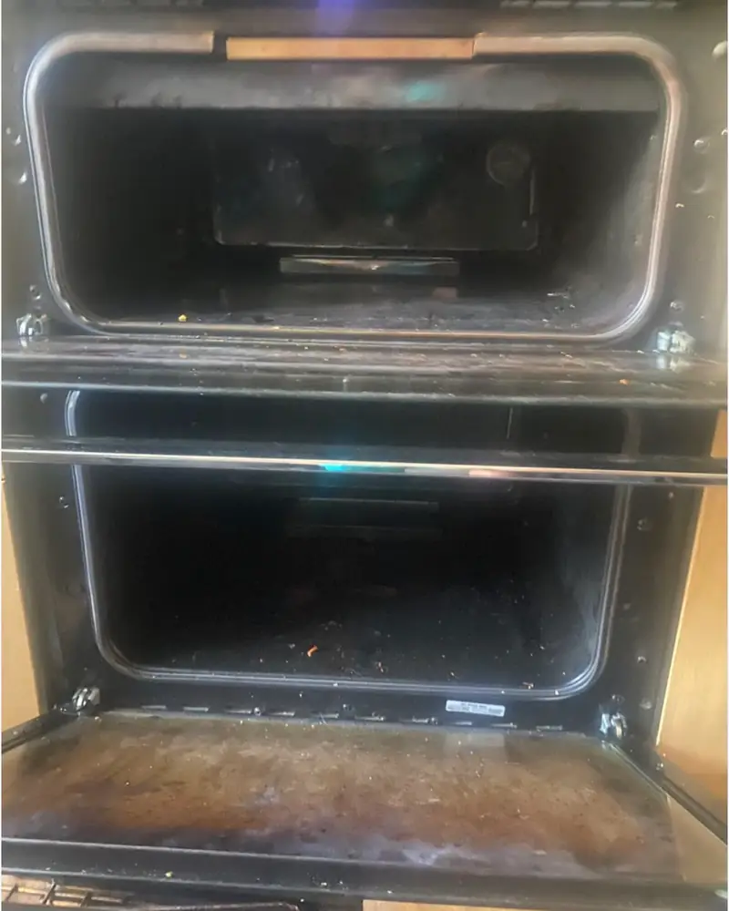 Double oven before cleaning, both doors open, with dark burnt-on grease inside both cavities and on the inner door